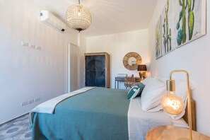 Une chambre à coucher avec un lit, un luminaire suspendu, un miroir fixé au mur et un tableau représentant un cactus.