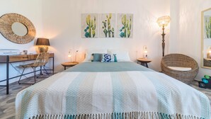 Un dormitorio con cama, escritorio, silla, lámpara y obras de arte en la pared.