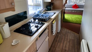 A compact kitchen with wooden cabinets, a stove, a sink, and a window overlooking a stone wall. - Ideal rural location for beaches, hills, forests, waterfalls and town (Bow Street)