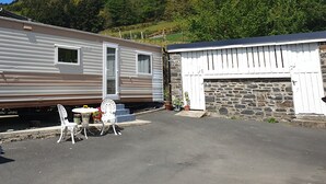 A mobile home with a patio area, a small table, and chairs. - Ideal rural location for beaches, hills, forests, waterfalls and town (Bow Street)