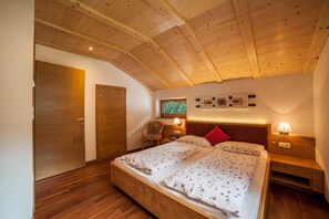 Camera da letto con soffitto in legno, due letti con lenzuola a motivi floreali, una sedia, lampade da comodino e una TV a parete.