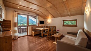 A cozy room with wooden floors, a sofa, a table with chairs, a bench, and a TV. - Apartment "Hahndl II" with Mountain View, Wi-Fi, Garden, Terrace and Balcony (St. Leonhard in Passeier Südtirol)