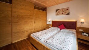 Una camera da letto con soffitto in legno, un letto con lenzuola a motivi floreali, un cuscino rosso, lampade da comodino e una radio.