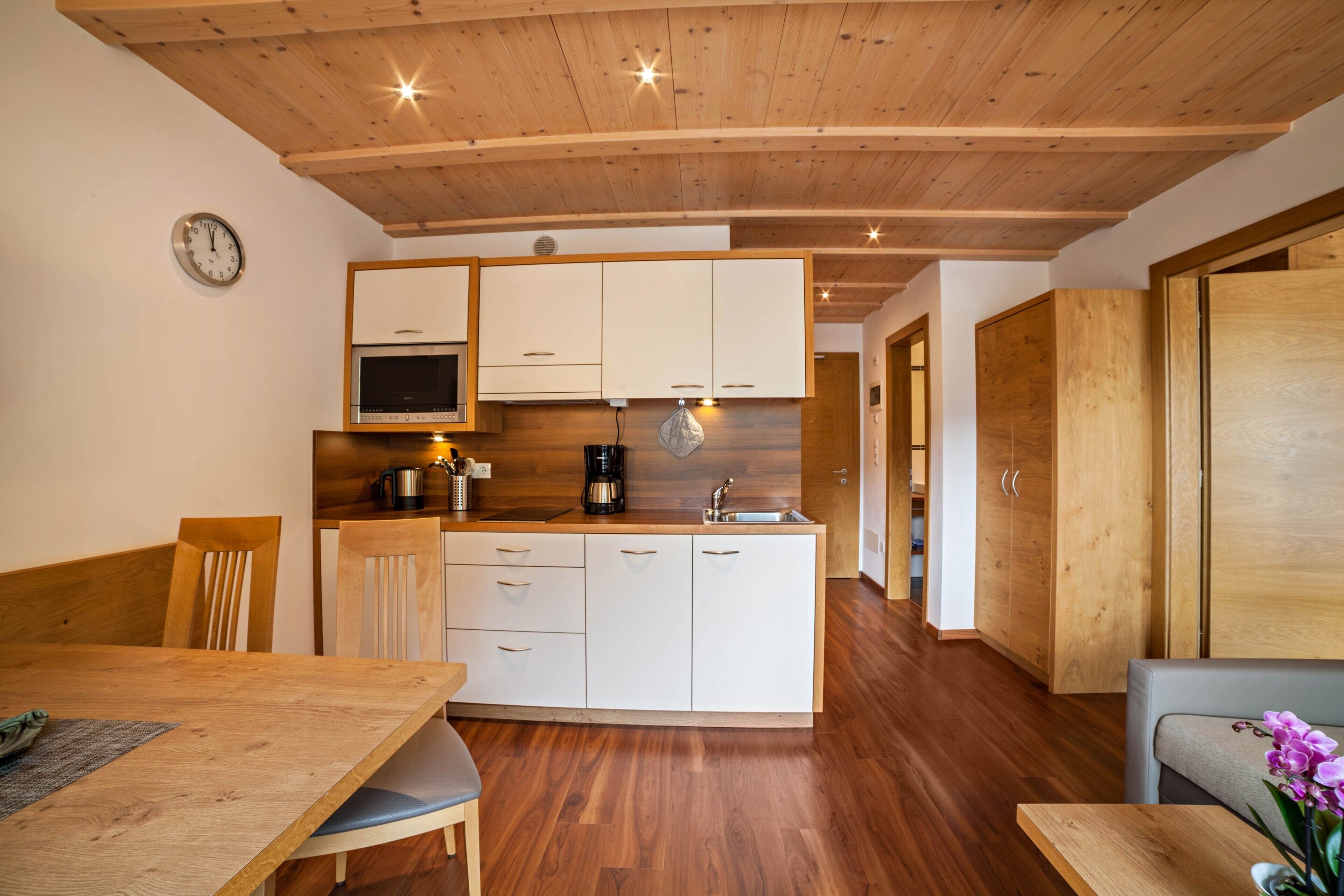 Een moderne keuken met houten kastjes, een eettafel, stoelen en een koffiezetapparaat.