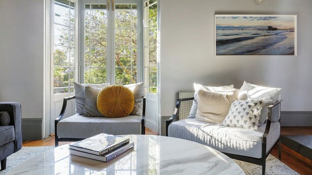 A living room with a large window, a white sofa, a round coffee table, and a framed picture on the wall. - Luxury Villas The Secret Garden (Pet Friendly) (Melbourne)