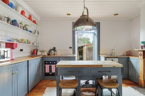 A kitchen with a central island, wooden cabinets, a hanging light fixture, and a view through a doorway. - Luxury Villas The Secret Garden (Pet Friendly) (Melbourne)