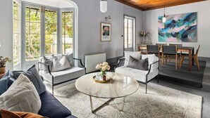 A spacious living room with a high ceiling, large windows, a dining area, and a modern art piece on the wall. - Luxury Villas The Secret Garden (Pet Friendly) (Melbourne)