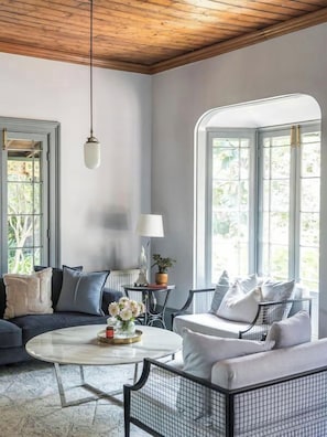 A room with a wooden ceiling, two large windows, a round coffee table, a sofa, and a chair. - Luxury Villas The Secret Garden (Pet Friendly) (Melbourne)