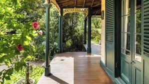 A covered wooden pathway leading to a building with green shutters, surrounded by lush greenery and flowering plants. - Luxury Villas The Secret Garden (Pet Friendly) (Melbourne)