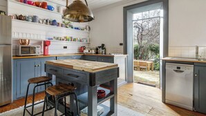 A kitchen with a wooden island, bar stools, a hanging light fixture, and a view of the outdoors. - Luxury Villas The Secret Garden (Pet Friendly) (Melbourne)