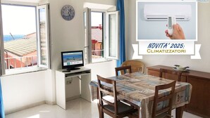 A room with a desk, a computer, a dining table with chairs, a clock on the wall, and a window with curtains. - La Casa di Rosa -  Apartment with Sea View in Rio Marina (Rio Marina)