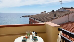 A balcony with a table set for two, overlooking a coastal view with buildings and a pier. - La Casa di Rosa -  Apartment with Sea View in Rio Marina (Rio Marina)