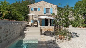 Uma casa de pedra com piscina, área de estar externa e alpendre coberto.