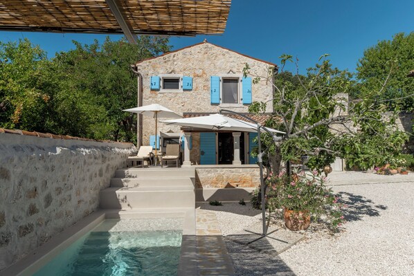 A stone house with a pool, outdoor seating, and a covered patio.