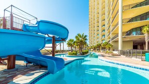 A swimming pool with a water slide and palm trees.