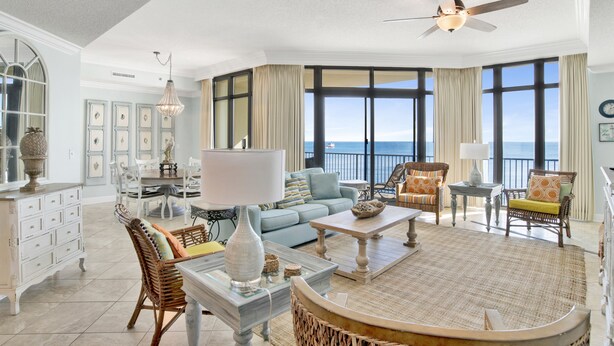 A spacious living room with a large window offering a view of the ocean, a ceiling fan, and a dining area with a table and chairs.