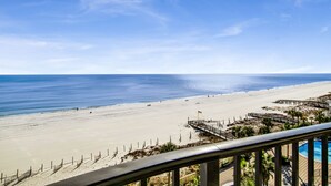A beach view from a balcony with a pool and a wooden deck.