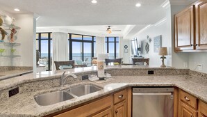 A modern kitchen with granite countertops, stainless steel sink, and wooden cabinets. There is a dining area with a view of the ocean.