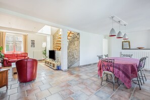 Un vaste espace de vie comprenant un canapé rouge, un téléviseur et un mur en pierre.
