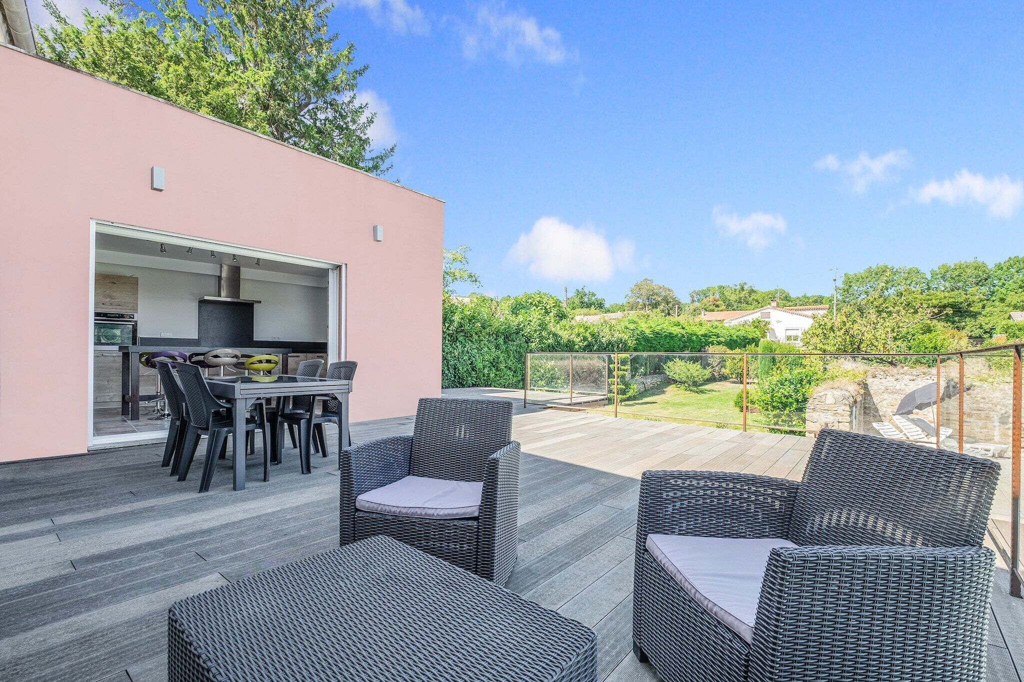 Une terrasse extérieure aménagée avec des meubles en osier et une table à manger, un coin cuisine et une vue sur un paysage verdoyant.