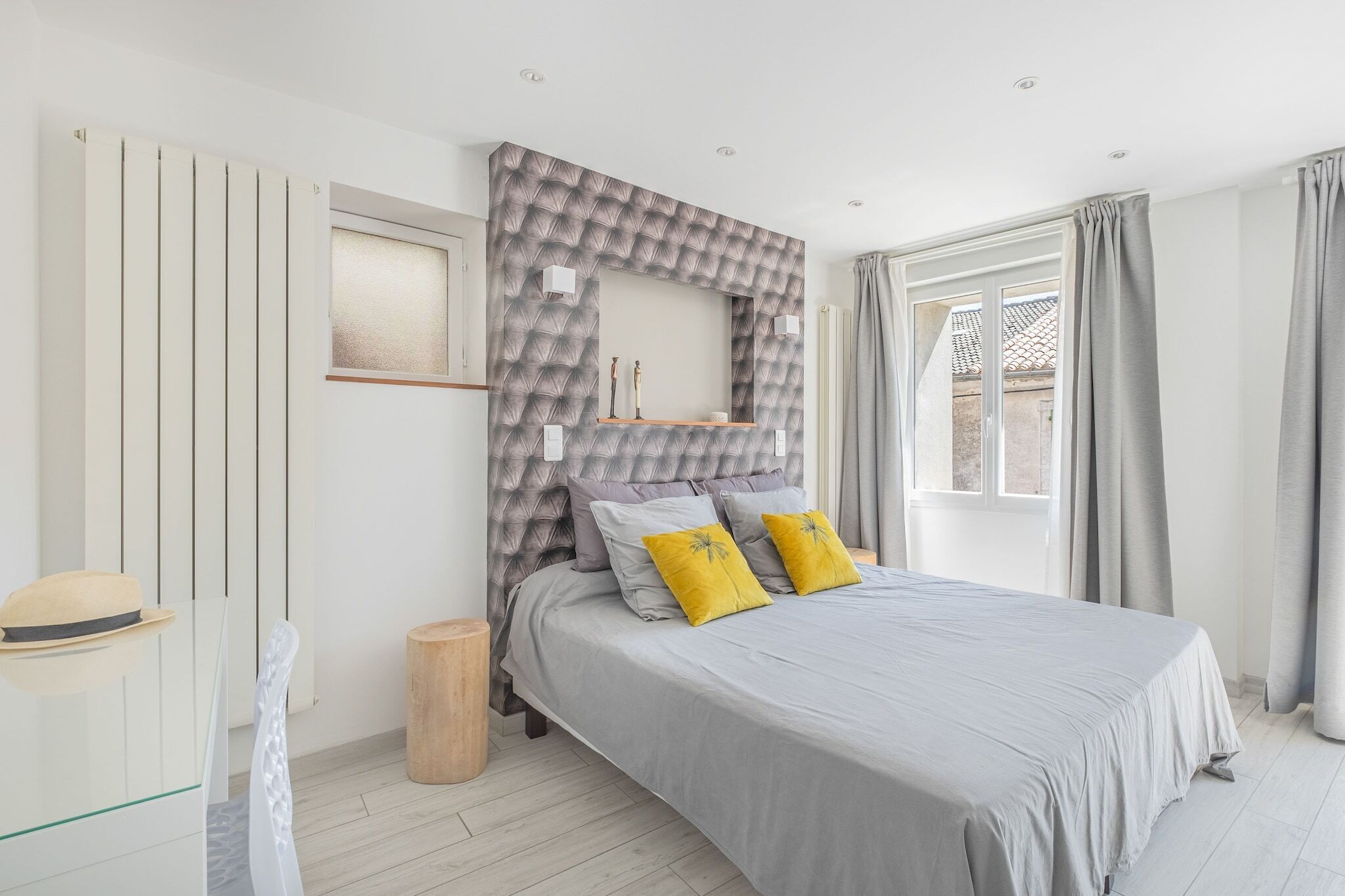A bedroom with a bed, a window, a radiator, and a mirror on the wall.