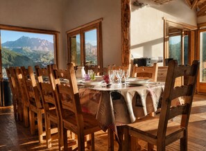 A dining area with wooden chairs and a table set for a meal, large windows offering mountain views, and a wooden ceiling.