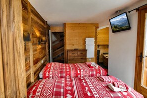 A wooden cabin bedroom with a bed, a nightstand, a dresser, and a TV mounted on the wall.