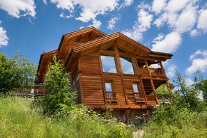 A wooden cabin with a balcony, surrounded by tall grass and trees.