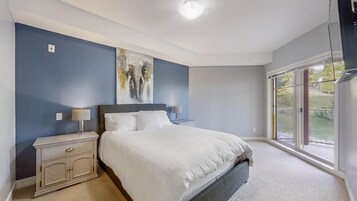 Un dormitorio con cama, mesitas de noche, un cuadro y un ventanal grande.