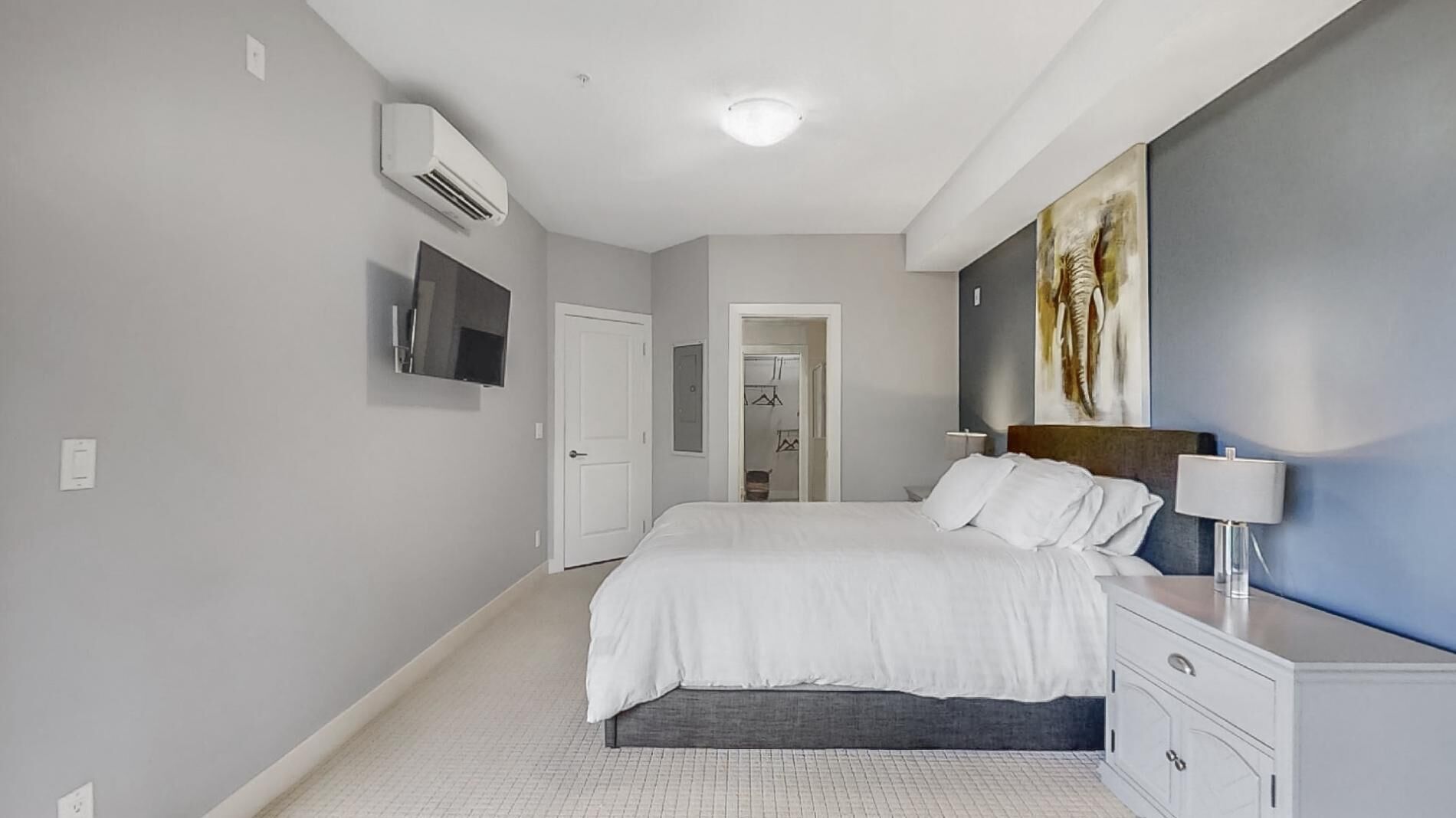 Un dormitorio moderno con cama, mesita de noche, lámpara y un cuadro grande en la pared.
