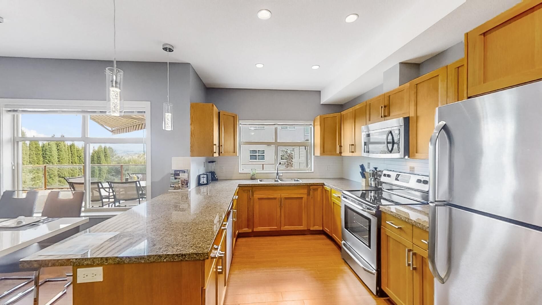 A modern kitchen with wooden cabinets, stainless steel appliances, and a large island with granite countertop.