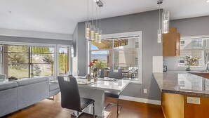 A modern kitchen with a large island, a dining area with a view, and a cozy seating area. - Okanagan Living at Copper Sky #104 (West Kelowna)