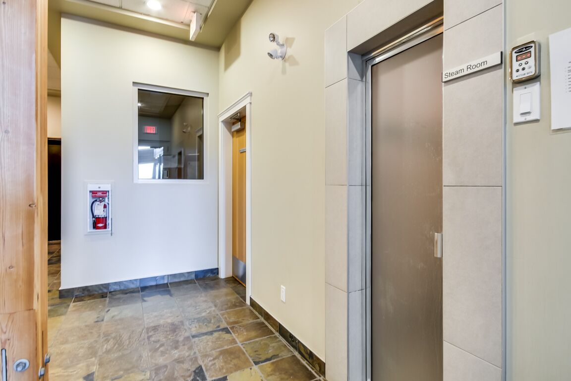 A hallway with a fire extinguisher, a steam room sign, and an elevator.