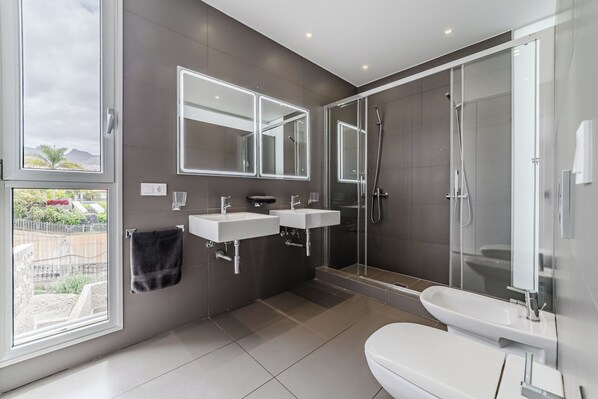 A modern bathroom with two sinks, a toilet, and a glass-enclosed shower.