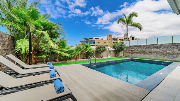 A swimming pool with lounge chairs and towels, surrounded by palm trees and a stone wall. - Modern 5B villa in El Duque, heated pool, wifi, just 250m from the beach (Costa Adeje)
