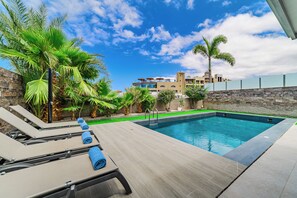 A swimming pool with lounge chairs and towels, surrounded by palm trees and a stone wall.