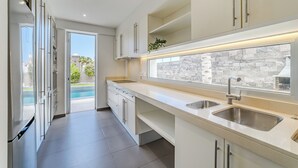 A modern kitchen with a large window, built-in shelves, and a view of a swimming pool. - Modern 5B villa in El Duque, heated pool, wifi, just 250m from the beach (Costa Adeje)