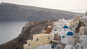 Un pueblo costero con edificios blancos y azules, acantilados rocosos y un mar tranquilo.