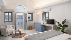 Amplia habitación con una cama grande, zona de estar con sofá y sillón, escritorio con televisor de pantalla plana y vista al mar a través de amplias ventanas.