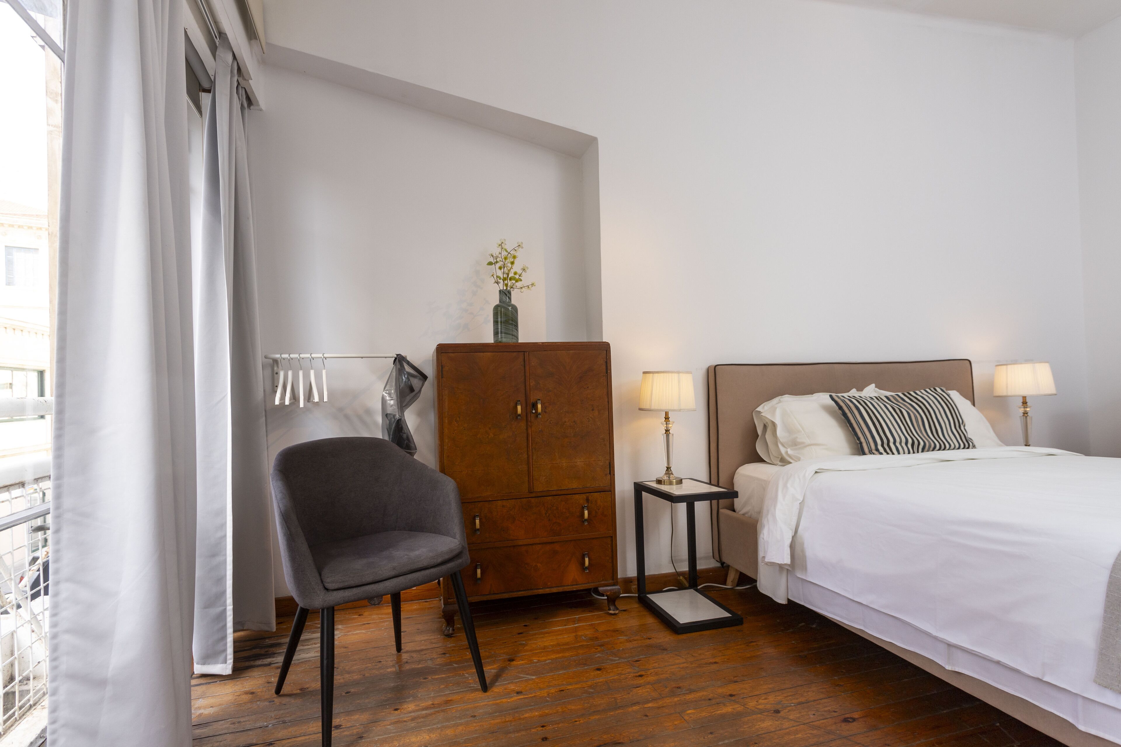 Une chambre d’hôtel avec un lit, une chaise, une armoire et une petite table avec une lampe.