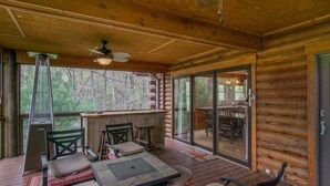 A wooden deck with a table and chairs, a bar area, and a sliding glass door leading to an outdoor seating area. - Blissful Bear Cabin, Long Range Views and 2 fireplaces (Brevard)