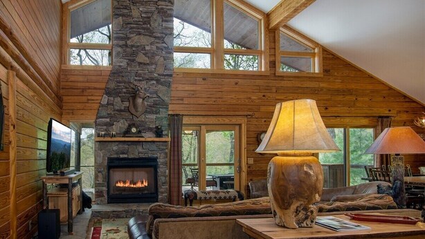 A log cabin interior with a stone fireplace, wooden walls, and large windows. - Blissful Bear Cabin, Long Range Views and 2 fireplaces (Brevard)