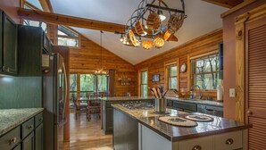 A kitchen with wooden walls, a central island, and a dining area with chairs. - Blissful Bear Cabin, Long Range Views and 2 fireplaces (Brevard)