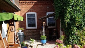 Eine Terrasse mit Blumentöpfen, einem Schaukelstuhl aus Holz und einem Tisch.