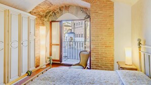 Un dormitorio con cama, una silla, una mesita de noche y vistas a un paisaje urbano a través de un arco.