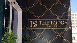 Entrada de un hotel con una pared negra que presenta patrones geométricos dorados y el nombre 'LS THE LODGE SUITES'.