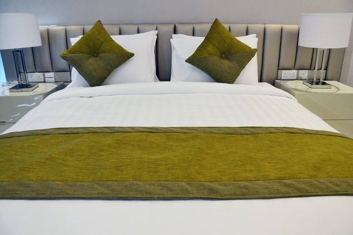 A neatly made bed with white linens and two green pillows, flanked by two bedside tables with lamps.