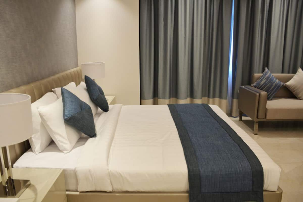 A hotel room with a bed, a nightstand, a lamp, a chair, and a window with curtains.