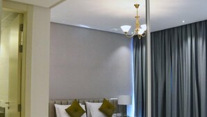 Una habitación de hotel moderna con una cama grande, una mesita de noche, una lámpara y vistas al exterior a través de un ventanal.
