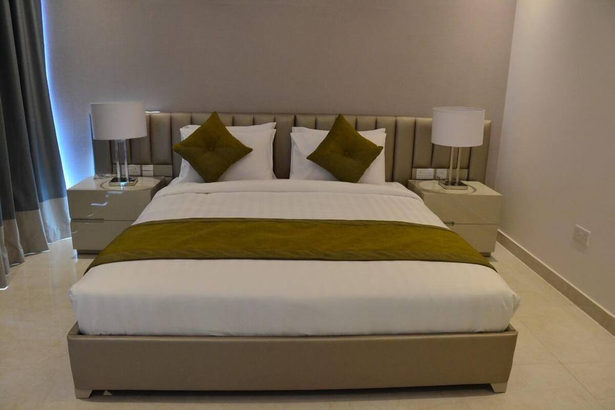 A neatly made bed with white linens and a green throw blanket, flanked by two bedside lamps on matching nightstands.